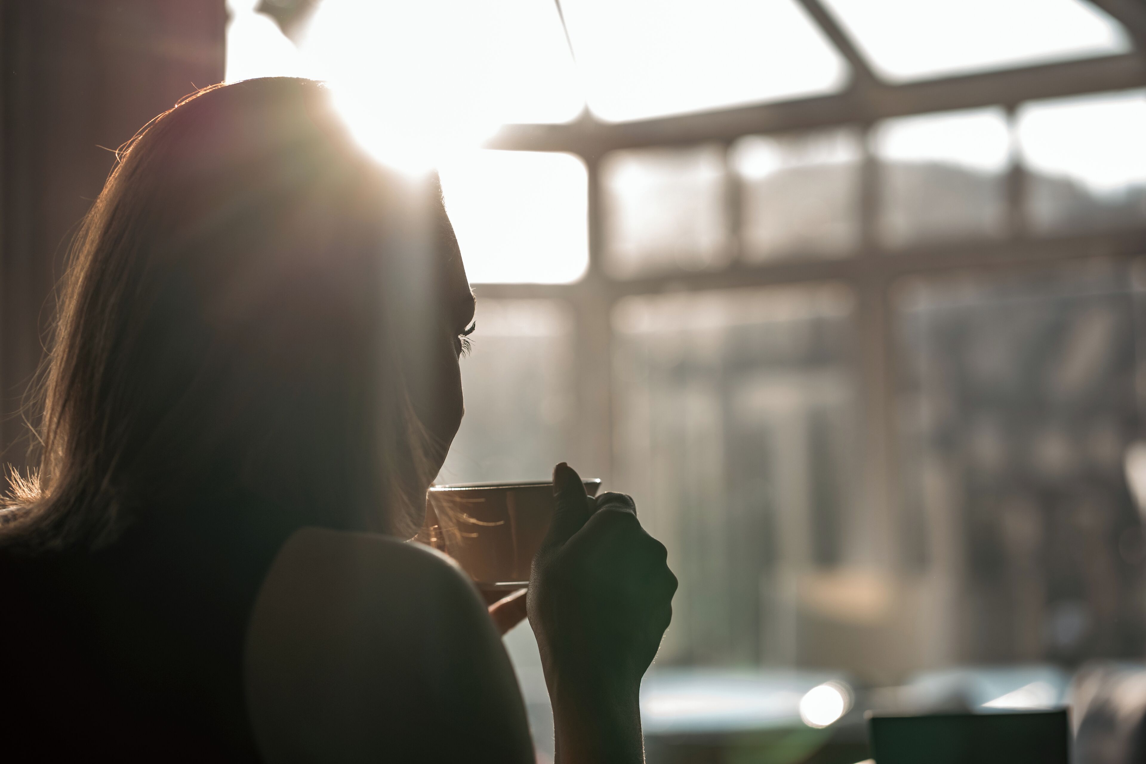 Una persona sosteniendo una taza, con luz solar entrando por una ventana.