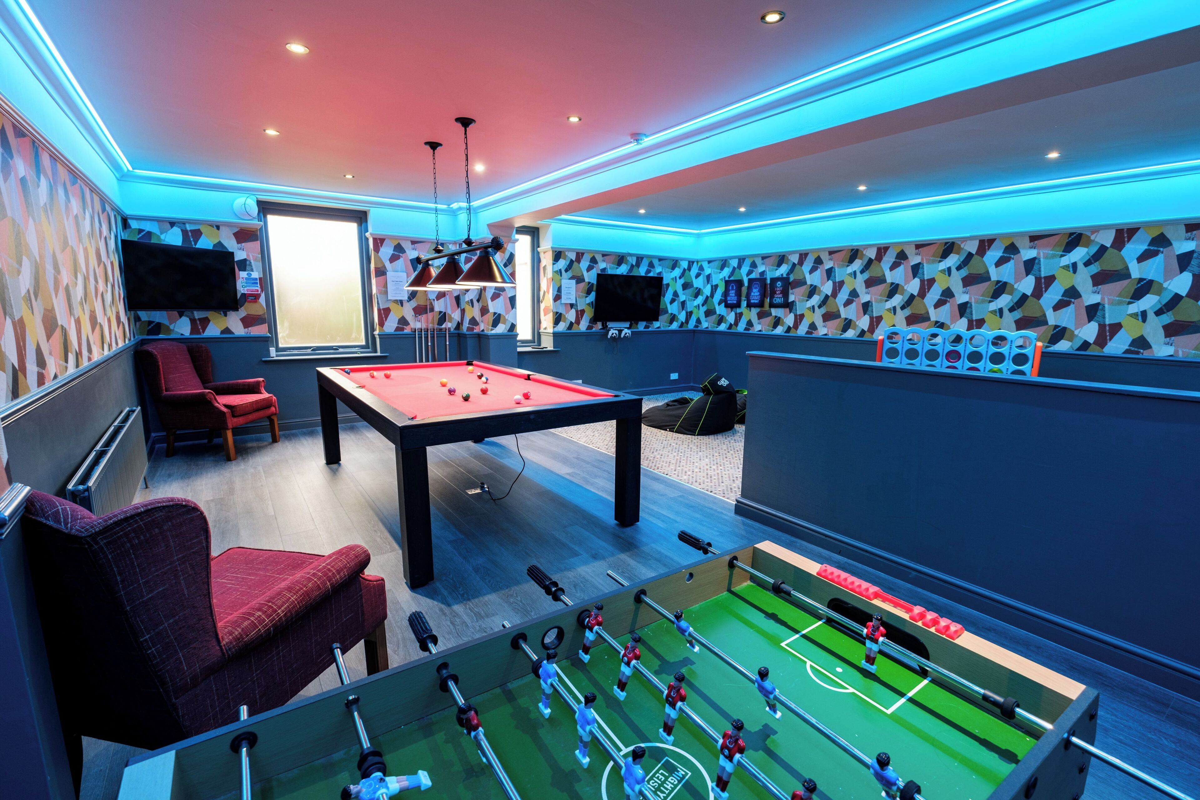 A room with a foosball table, a pool table, and a red sofa.