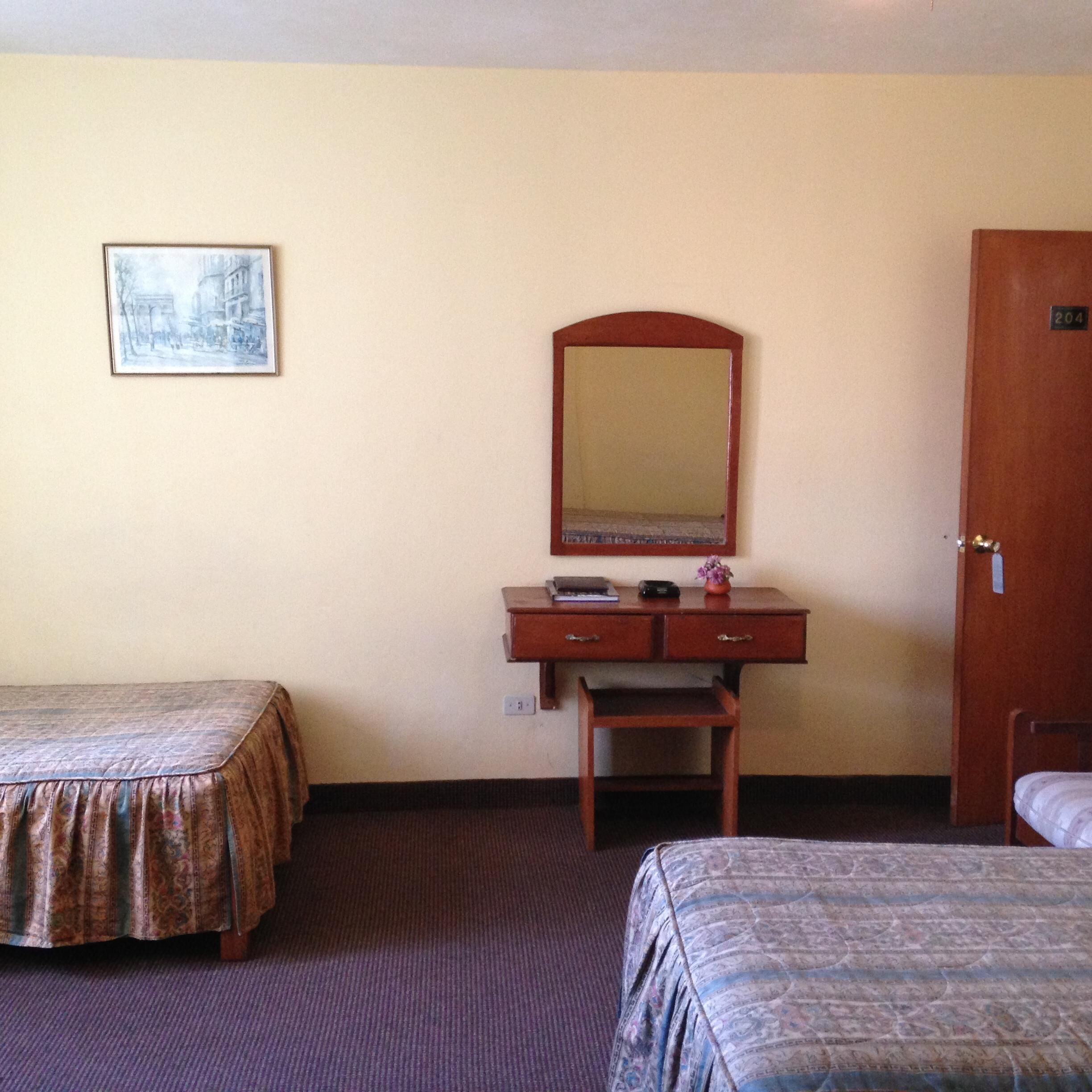 A hotel room with two beds, a desk with a mirror, and a door.