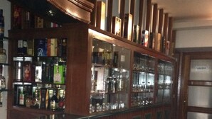 A bar area with shelves of liquor bottles and glasses, a tiled floor, and a wooden counter with decorative panels. - Hotel Regency (Lima)