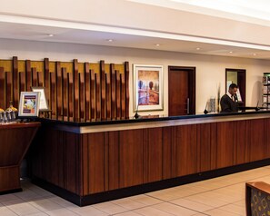 A reception desk with a wooden panel design, a framed artwork, and a digital information board. - City Lodge Hotel Pinelands, Cape Town (Cape Town)