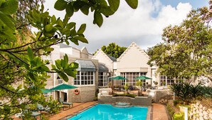 A swimming pool with a stone border, surrounded by a patio area with chairs and umbrellas.