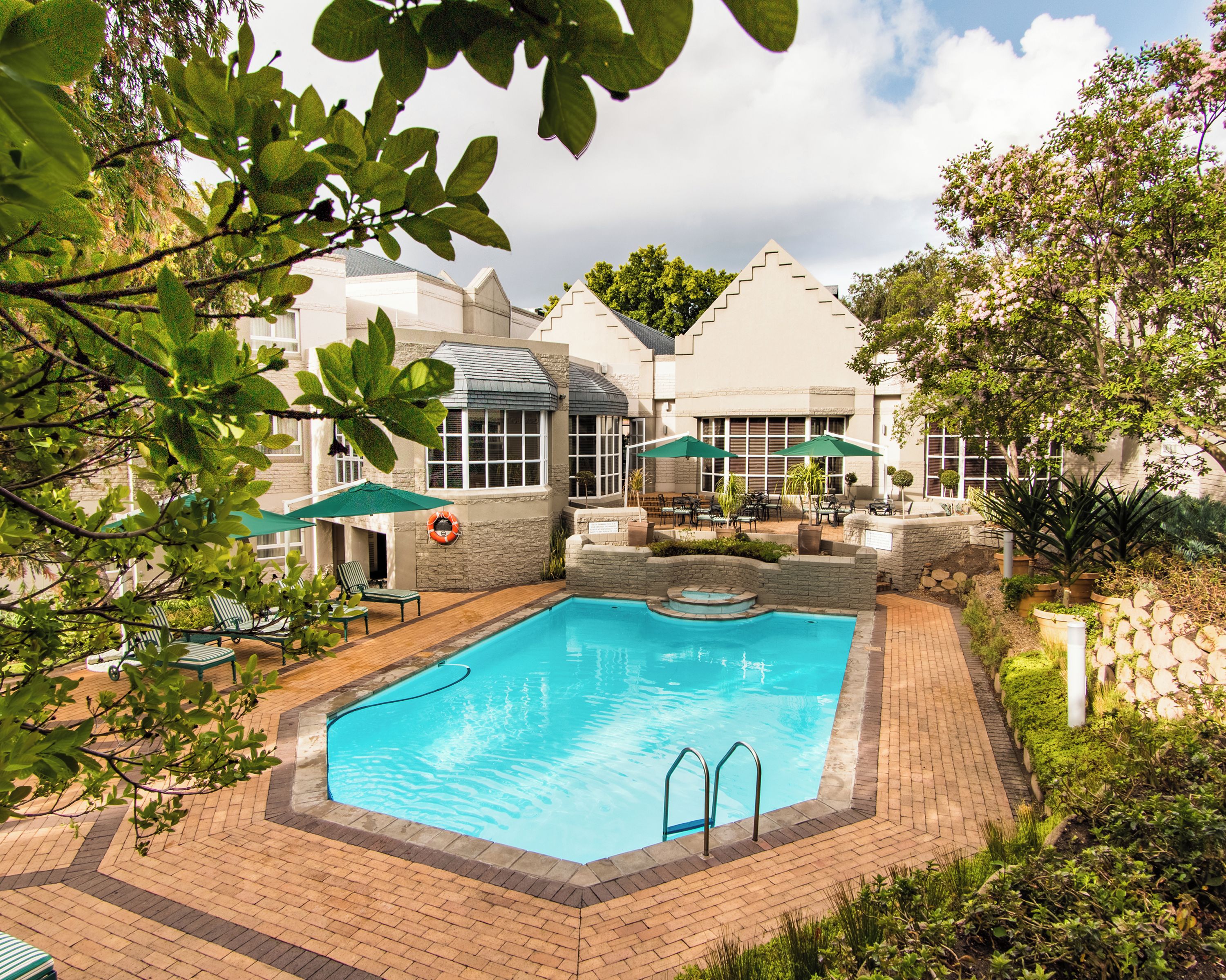 A swimming pool with a stone border, surrounded by a patio area with chairs and umbrellas.