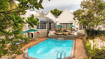 A swimming pool with a stone border, surrounded by a patio area with chairs and umbrellas.