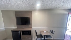 Une pièce compacte comprenant un coin cuisine, un téléviseur à écran plat fixé au mur, une table à manger avec deux chaises et une porte donnant sur un espace extérieur.