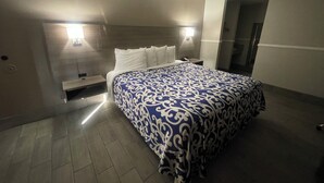 Une chambre d’hôtel avec un grand lit, deux tables de chevet, une commode, une lampe fixée au mur et une porte donnant sur une autre pièce.