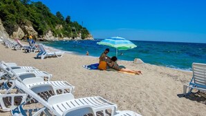 En strand med hvide liggestole og en stribet parasol.