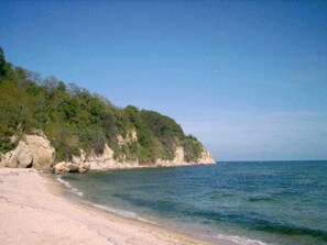 Una playa con agua cristalina, una orilla arenosa y un acantilado rocoso con vegetación.