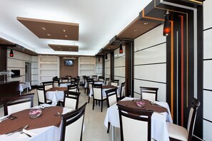 Un restaurante con varias mesas, sillas y una pantalla de televisión en la pared.