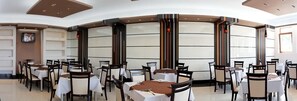 Un restaurant amb taules rodones, cadires i un televisor a la paret.