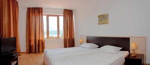 A hotel room with a bed, a television, a window with curtains, and a wall-mounted picture. - Vemara Club (Byala)