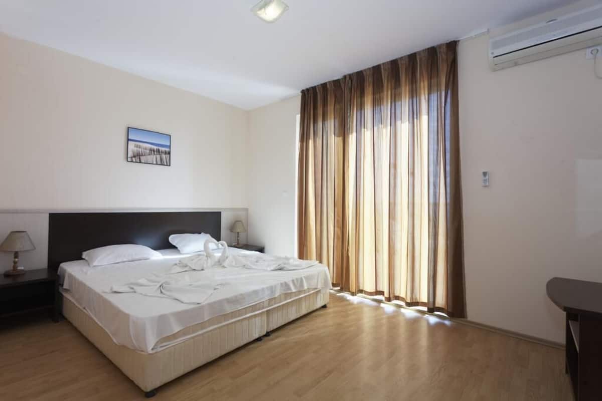 A hotel room with a large bed, a nightstand with a lamp, a picture on the wall, and a window with curtains.
