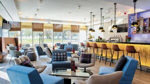 A modern hotel lobby with seating areas, a bar, and large windows. - Leonardo Hotel Hannover (Hannover)