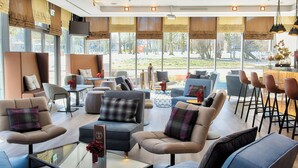 A modern hotel lobby with seating areas, a bar, and large windows offering a view of the outdoors. - Leonardo Hotel Hannover (Hannover)