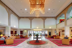Un hall d’entrée spacieux avec une table ronde centrale, des coins salon et un lustre.