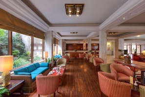 A spacious lounge area with a long table set for dining, comfortable seating, and large windows offering a view of the outdoors. - Himalaya (Lalitpur)