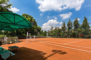 A tennis court with a net, a green canopy, and a stone wall. - Himalaya (Lalitpur)