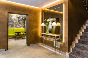 Un interior moderno con una escalera, una consola con lámparas y un área de estar con un sofá verde y sillones.