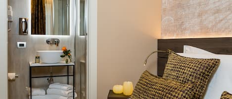 A hotel room with a bed, a bedside table with a lamp, a bathroom with a sink and mirror, and a wall with a textured design.