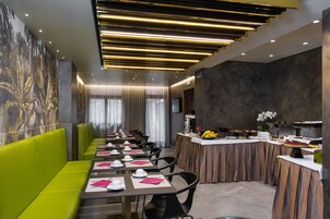 Un comedor moderno con asientos tipo banca verdes, mesas largas y una cocina central.