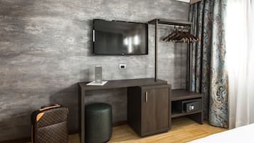 Una habitación de hotel moderna con un televisor de pantalla plana montado en una pared texturizada, un escritorio de madera oscura con un pequeño armario, una maleta y un reposapiés redondo.