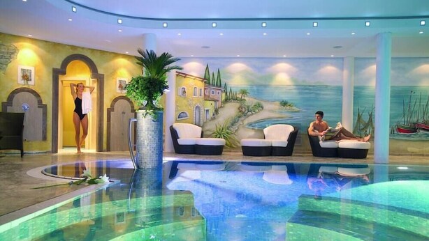 A hotel lobby with a pool, seating areas, and a mural of a coastal scene.