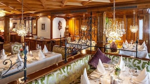 A restaurant with wooden paneling, chandeliers, and a green patterned bench.