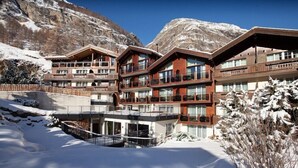 A multi-story hotel with balconies, a ski lift, and a snowy mountain backdrop.