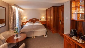 A hotel room with a bed, bedside lamps, a wooden wardrobe, a small table with a vase, and a coffee machine.