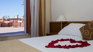 Habitación de hotel con cama, mesita de noche, lámpara y vistas al balcón exterior.