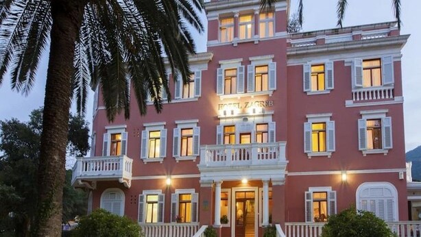 Un hotel de varios pisos con fachada rosa, adornos blancos y balcones.