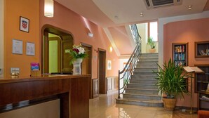 Zona de recepción de un hotel con un mostrador de madera, una escalera y una estantería.