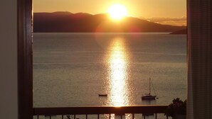 A sunset over a calm sea with boats, viewed from a window with a wooden frame. - John & George (Nafplio)