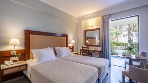 A hotel room with two beds, a desk, a chair, and a balcony with a view. - John & George (Nafplio)