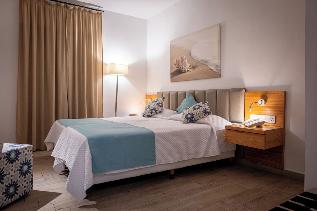 Une chambre d’hôtel bien rangée, avec un lit, une table de chevet, une lampe et un tableau au mur.