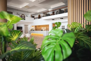 Eine geräumige Lobby mit einer Rezeption, mehreren Sitzbereichen und einem Balkon im zweiten Stock.