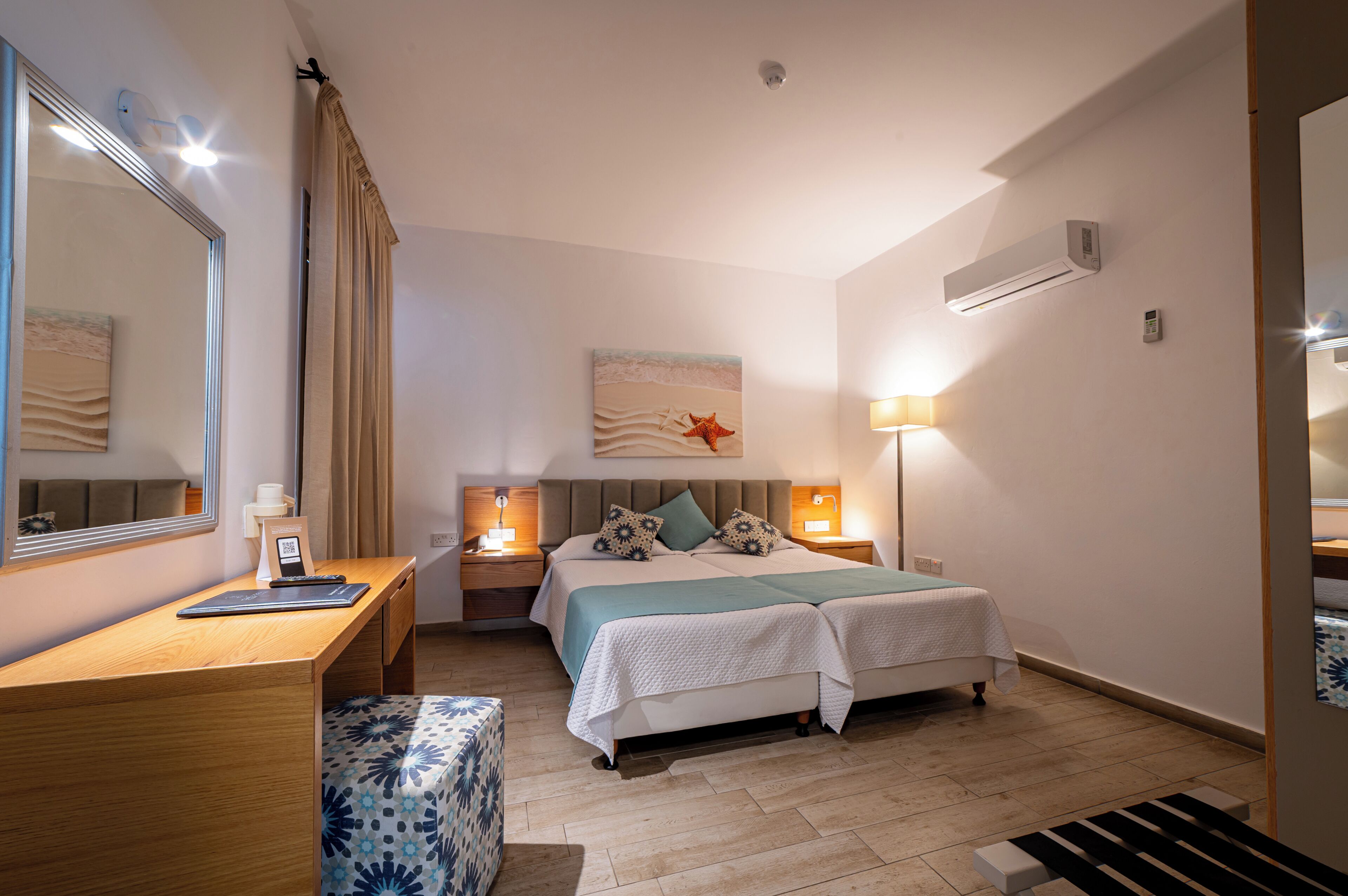 A bedroom with a bed, bedside tables, a desk, a chair, a mirror, and a wall-mounted air conditioner.