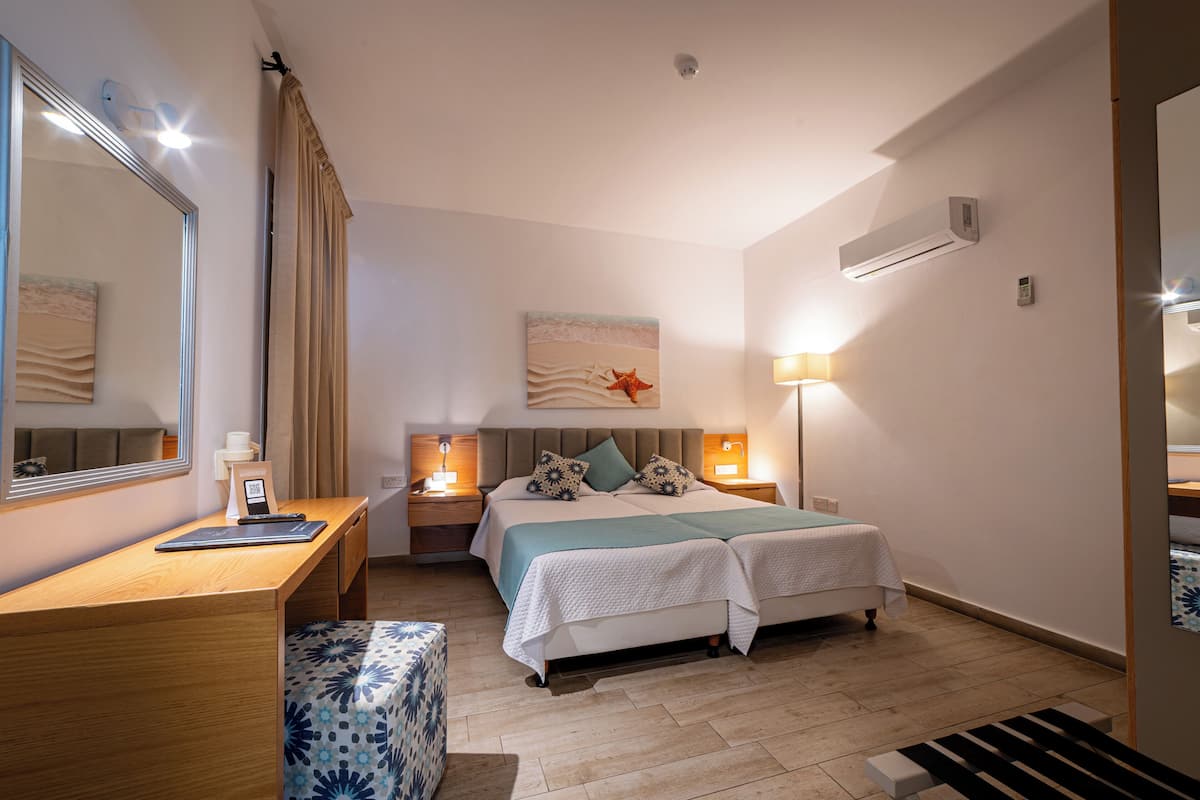 Une chambre à coucher comprenant un lit, des tables de chevet, un bureau, une chaise, un miroir et un climatiseur fixé au mur.