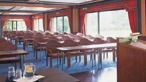 Ett konferensrum med rader av stolar och bord, stora fönster och ett trägolv.