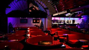 Ett svagt upplyst loungeområde med röda sittplatser och en bar i bakgrunden.