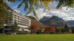 Ett hotell med modern design, en stor gräsmatta och berg i bakgrunden.