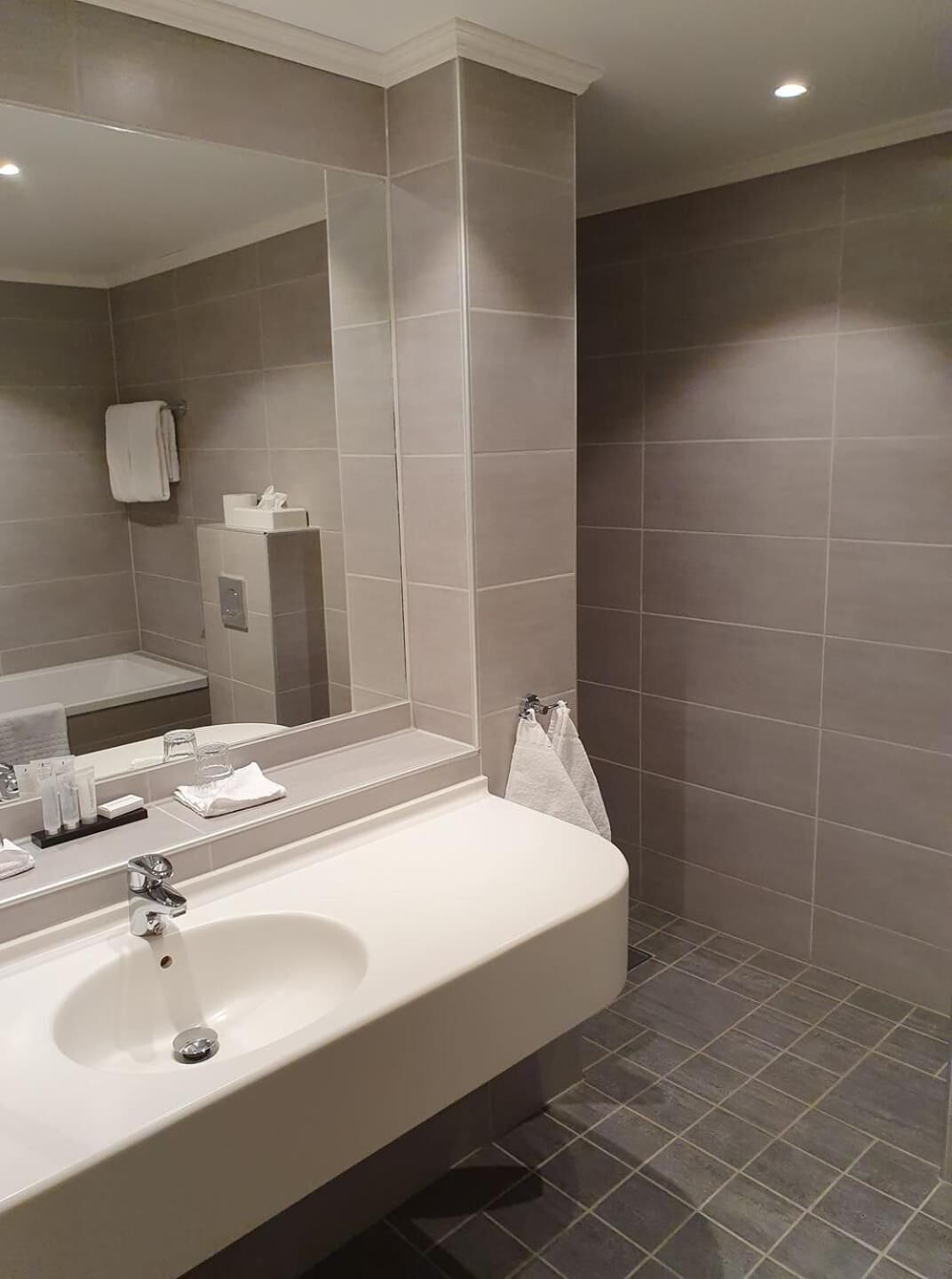 Un baño moderno con un espejo grande, un lavabo blanco y una zona de ducha.