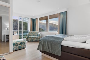 A bedroom with a bed, a chair, a view of mountains, and a large window.