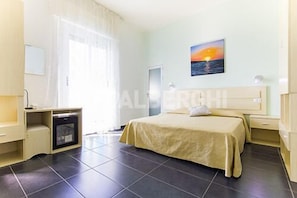 A hotel room with a bed, a desk, a chair, a small table, and a painting on the wall. - MoMo Seaview Hotel Rimini (Rimini)