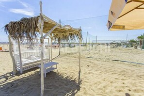 A beach umbrella, a beach chair, and a thatched roof structure on a sandy beach. - MoMo Seaview Hotel Rimini (Rimini)