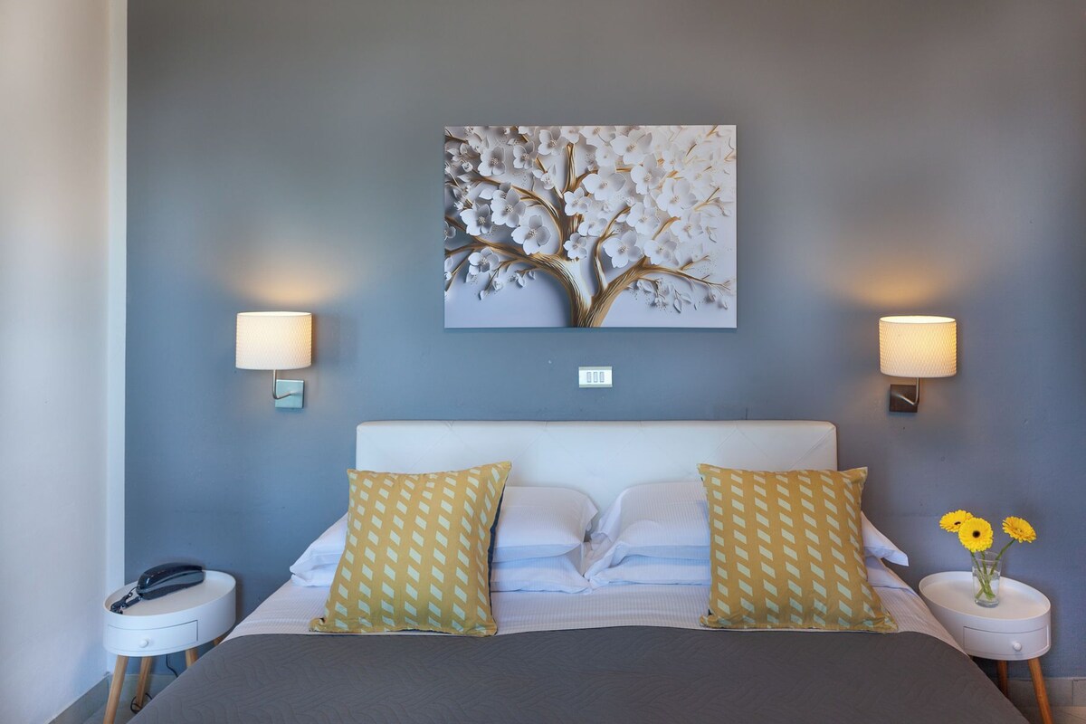 Un dormitorio con una cama, dos mesitas de noche, una lámpara de pared y una obra de arte floral.