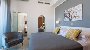 A hotel room with a large bed, a sofa, a painting on the wall, and a bathroom visible through an archway. - MoMo Seaview Hotel Rimini (Rimini)