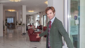 A man in a green jacket and plaid tie standing in a modern lobby with marble floors, leather furniture, and a glass door with a sign. - MoMo Seaview Hotel Rimini (Rimini)