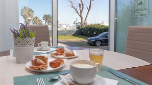 A table with pastries, a cup of coffee, and a glass of tea, with a view of palm trees and a car outside. - MoMo Seaview Hotel Rimini (Rimini)
