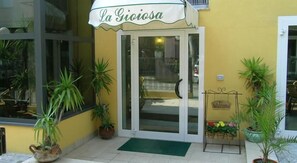 A yellow building with a white awning labeled "La Gioiosa." There are potted plants outside and a welcome sign on the right. - Hotel La Gioiosa (Rimini)